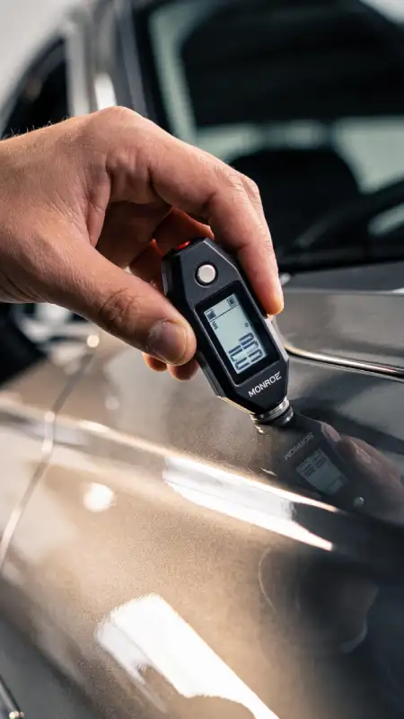 کارشناس خودرو در حال استفاده از دستگاه ضخامت سنج رنگ برای تشخیص رنگ شدگی بدنه